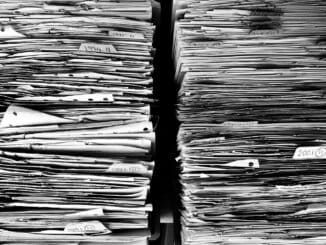 Paperwork stacked beside a laptop as in-house lawyers sort AI-drafted complaints