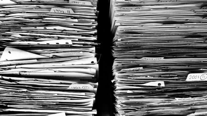 Paperwork stacked beside a laptop as in-house lawyers sort AI-drafted complaints