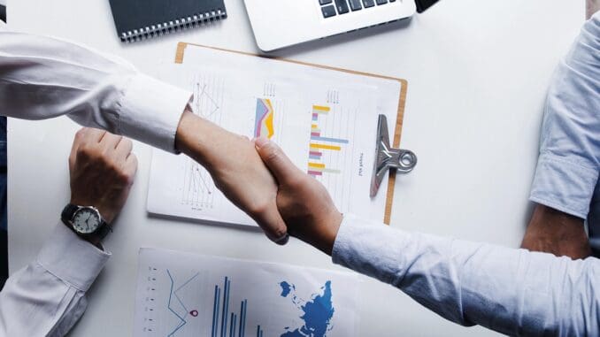 Handshake across an office desk, the end point of in-house legal hiring Handshake across an office desk, the end point of in-house legal hiring